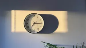 Analoginis laikrodis ant sienos su žaliai apšviestu šviesos ruožu, simbolizuojantis laiką.