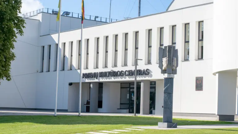 Šiuolaikinis valstybinės institucijos pastatas su Lietuvos vėliava saulėtą dieną.