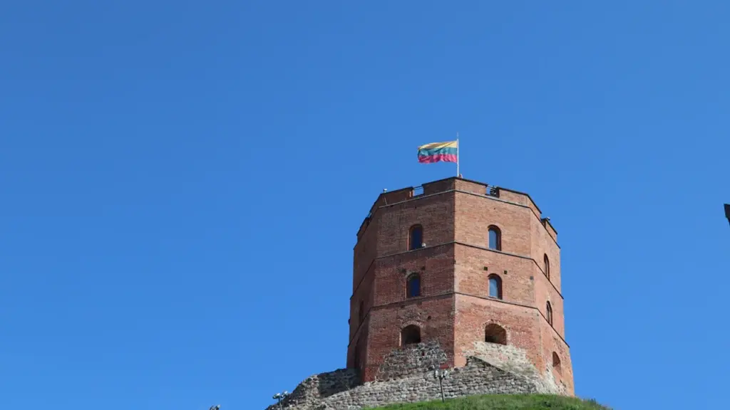 Gedimino pilies bokštas su Lietuvos vėliava ant žalio kalno, žydrame danguje.