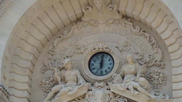 Senovinis laikrodis su klasikinėmis skulptūromis istorinės architektūros fone ramiam apmąstymui.